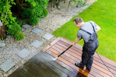 Power washing - man cleaning terrace with a power washer - high water pressure cleaner on wooden terrace surface - how to
