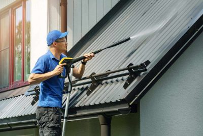 Man standing on ladder and cleaning house metal roof with high pressure washer - how to properly seal your roof