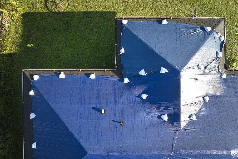Aerial view of a damaged roof covered with a blue protective tarp