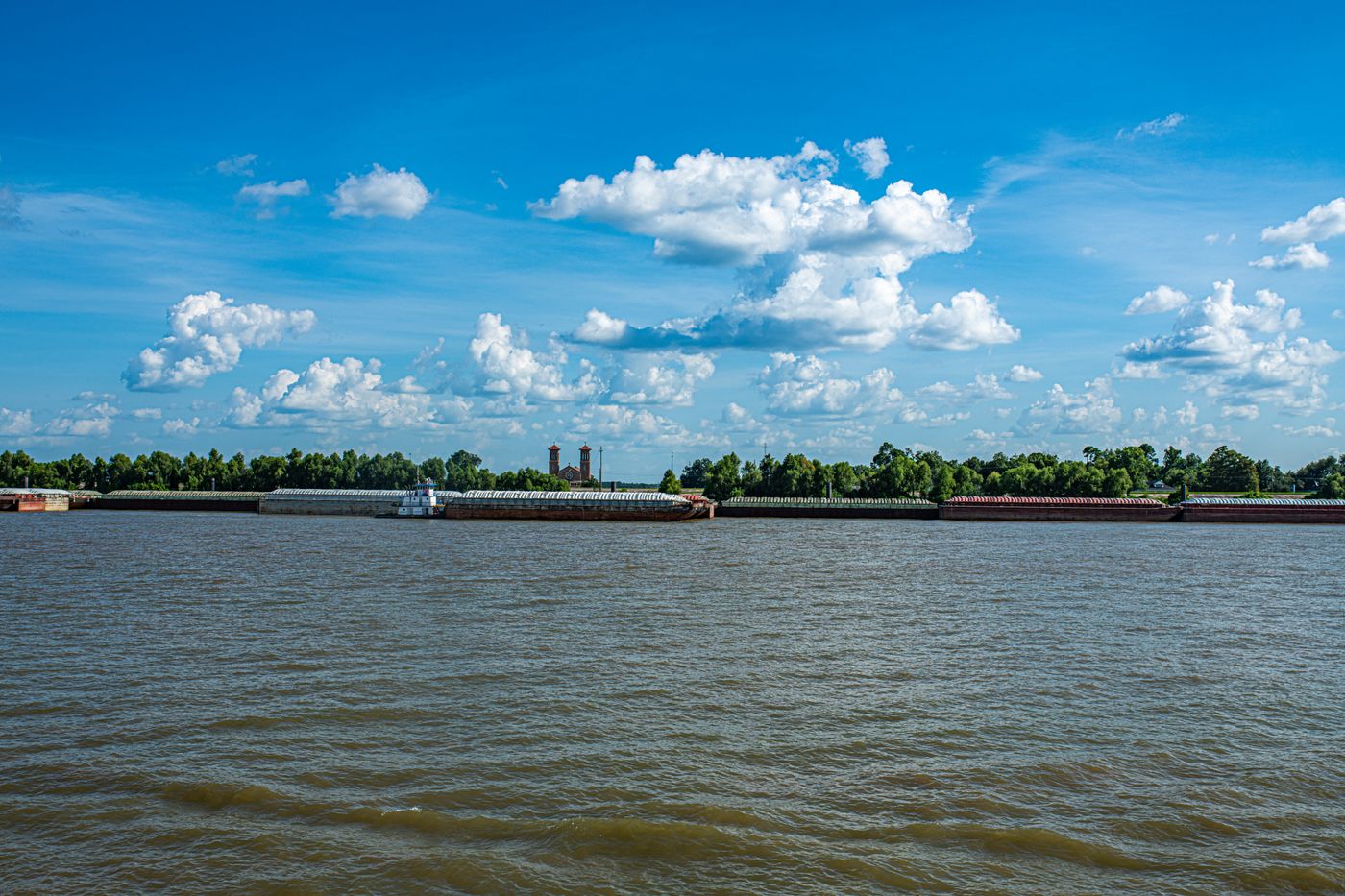 Barges on a wide river under a blue sky