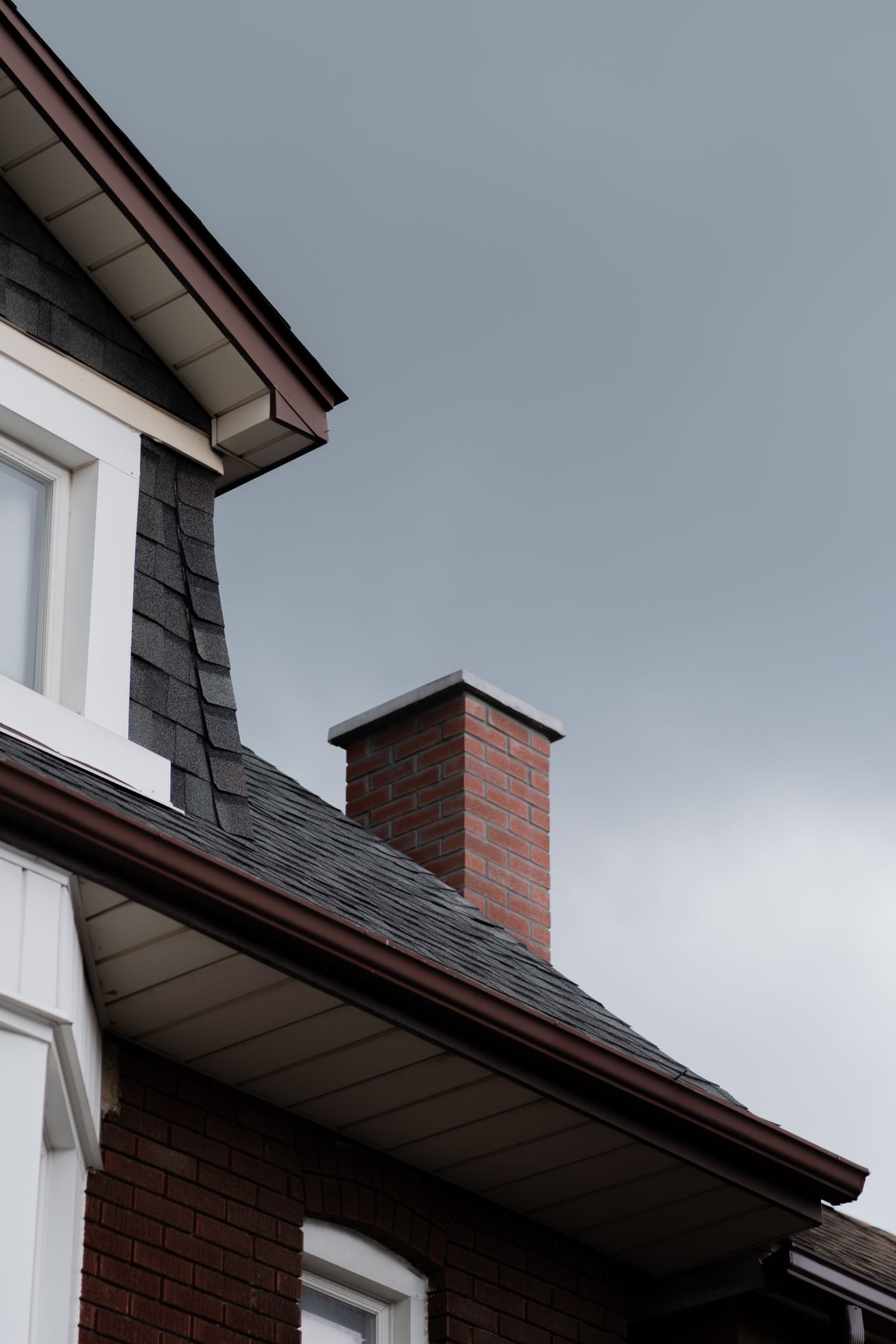Dark shingle roof above a brick wall and chimney