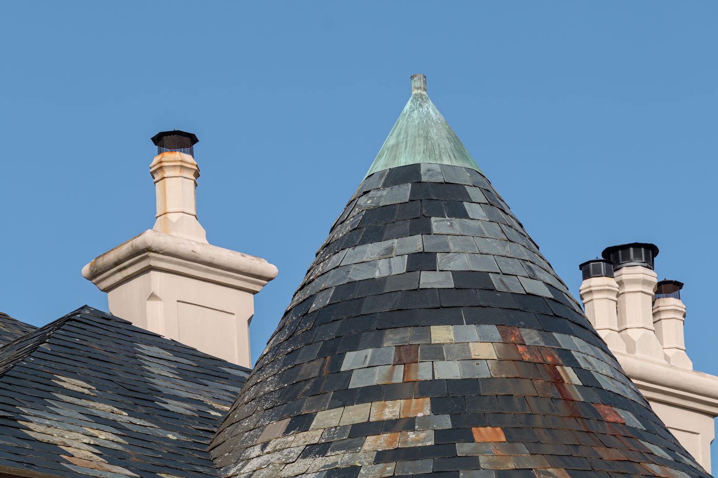 Multicolored slate turret beside white chimneys
