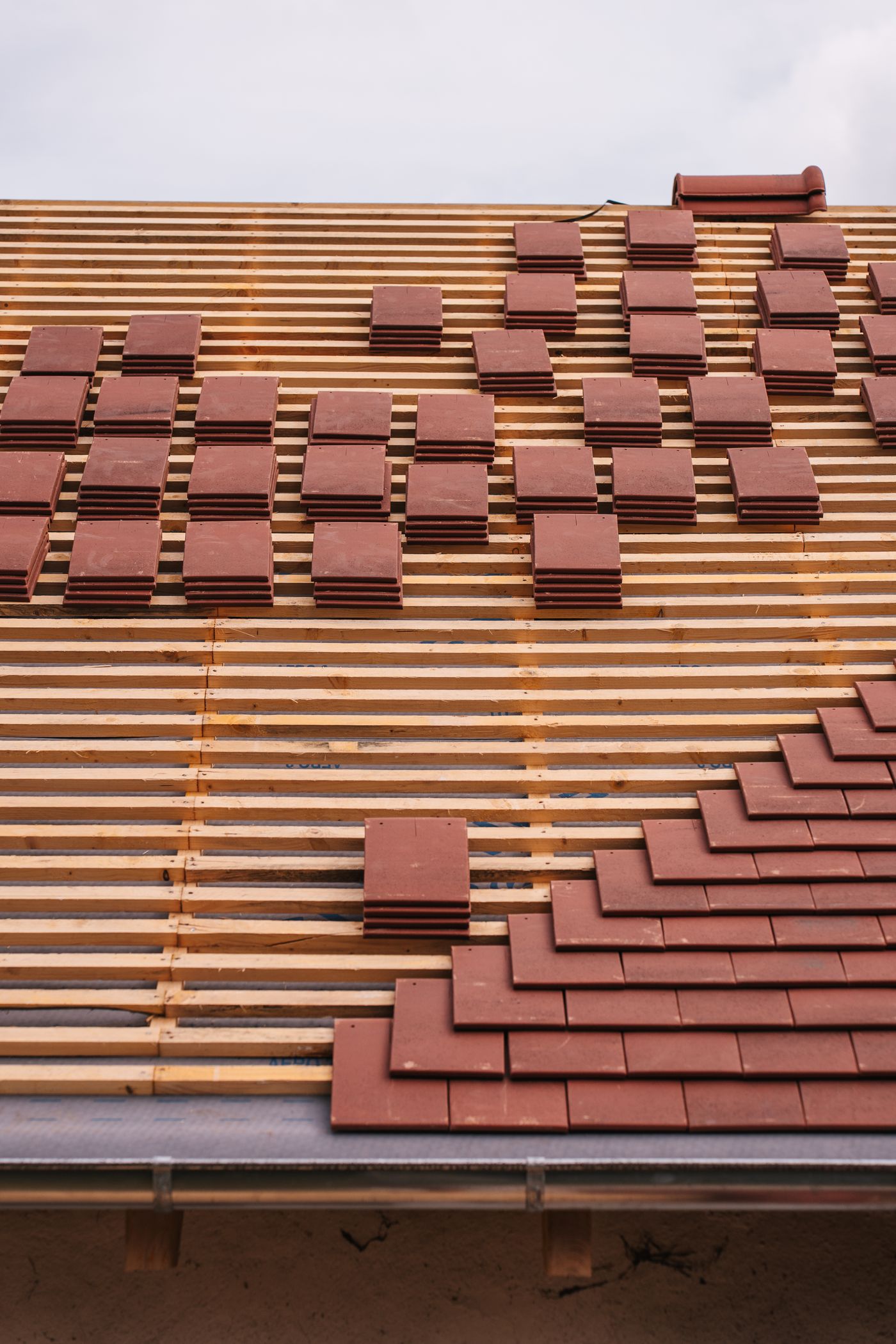 Red clay tiles stacked on roof battens during installation
