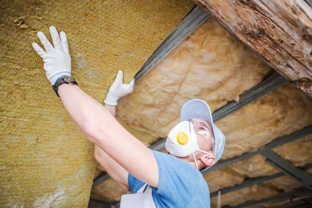Installer fitting insulation between attic rafters