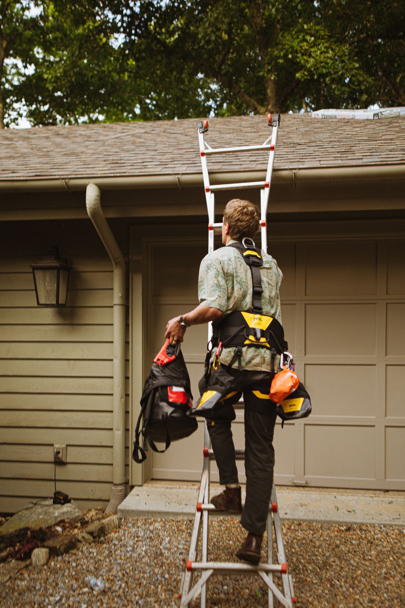 Roofer in a safety harness climbing a ladder to a house roof