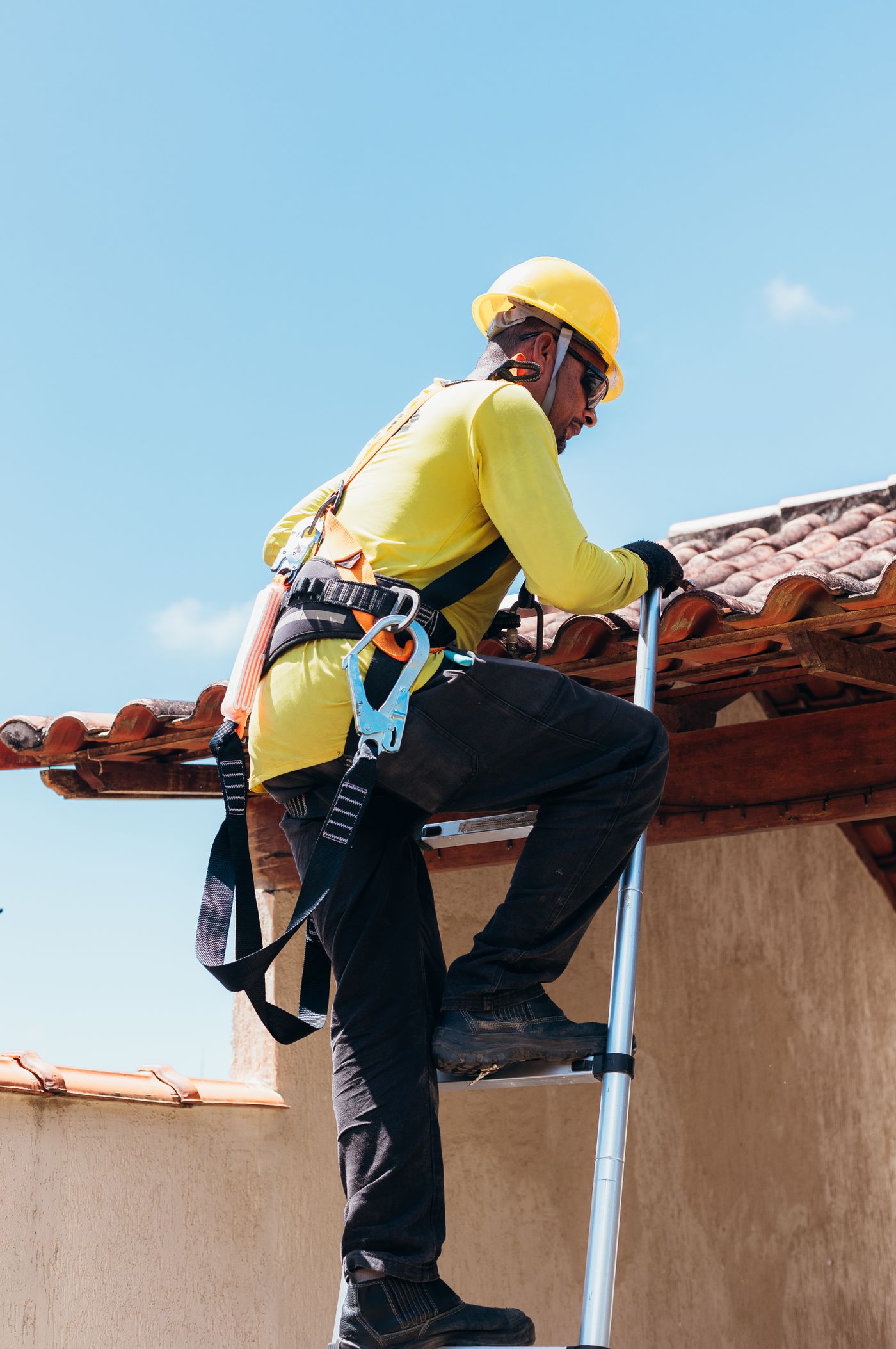 Roofer in a safety harness climbing onto a tile roof