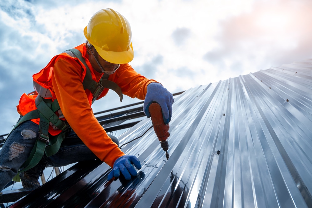 Roofer in a harness fixing metal roof panels