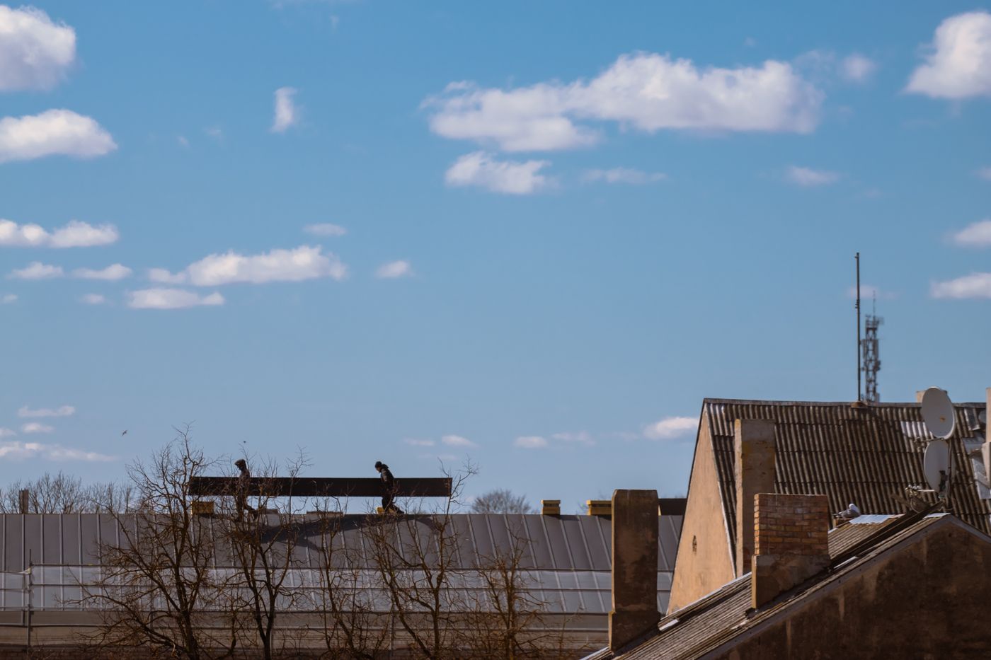 Roofers carrying a beam across a rooftop