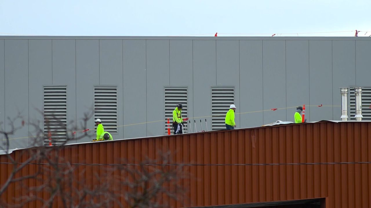 Roofing crew in hard hats and hi-vis working a metal commercial roof on a safety line