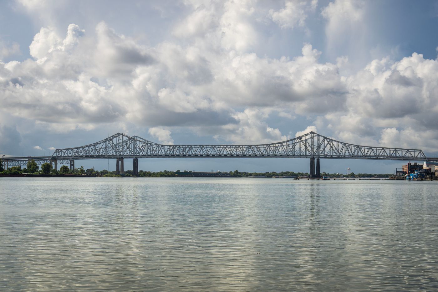 Truss bridge over a wide river under clouds