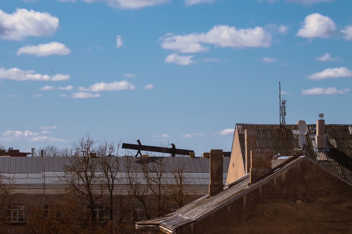 Two roofers carrying materials across a rooftop