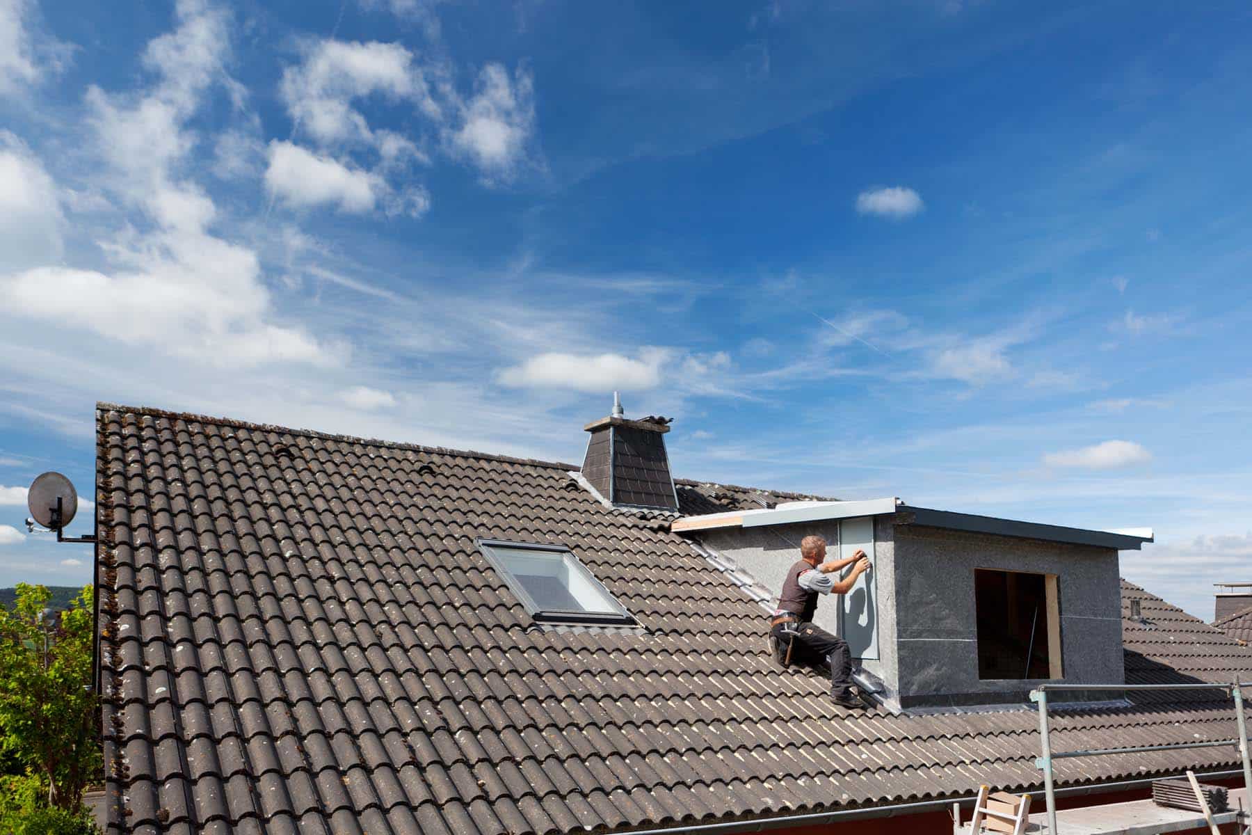View of a rooftop with a working roofer assembling pieces to the dormer wall